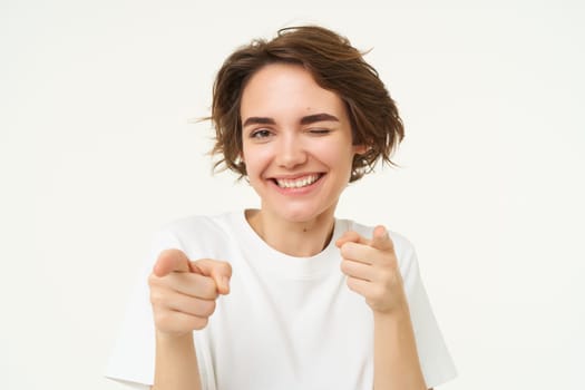 You got this. Smiling, cheerful and confident woman, encourages you, points fingers at camera, invites you, stands over white studio background.