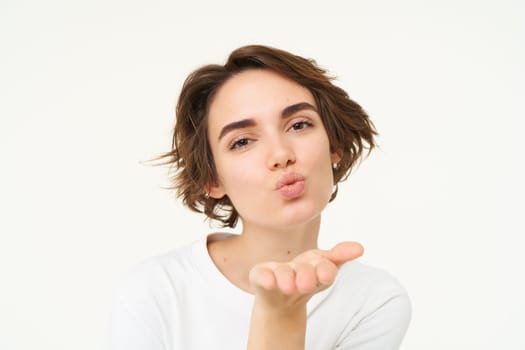 Close up of brunette woman, sending air kiss at camera, posing over white background.
