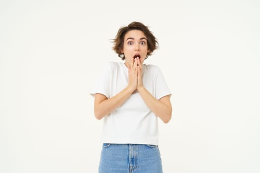 Portrait of brunette woman with shocked, amazed face, drops jaw and gasps worried, looking at camera, isolated over white background.