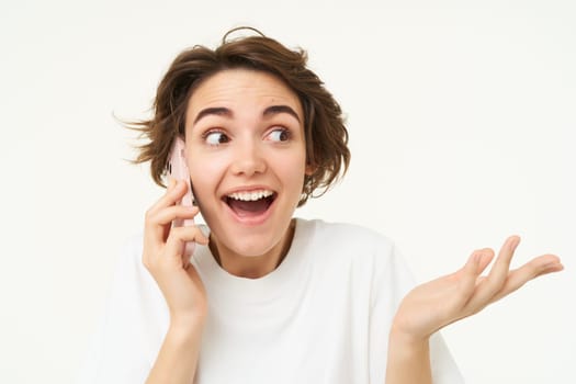 Excited brunette woman celebrating, answers phone call and looking happy, winning, triumphing from great big news, standing over white background.