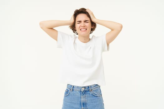 Portrait of troubled woman, holds hands on head and panicking, feeling upset, depressed, stands over white studio background.