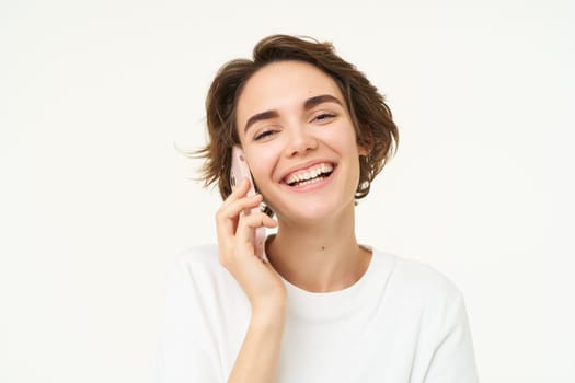 Portrait of happy, chatty young woman talking on mobile phone, using smartphone, calling someone, standing over white studio background.