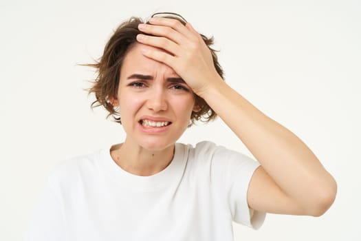 Portrait of woman touches her head, looks upset or disappointed, forgot something, has headache, migraine, standing over white background.