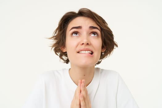Close up of hopeful young woman pleading, holding hands in pray, begging for wish come true, isolated against white background.