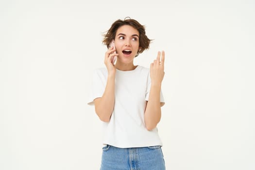 Portrait of chatty young woman, talking on mobile phone and gesturing, discussing something over the telephone conversation, standing over white background.