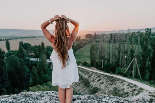 Romantic beautiful bride in white dress posing with sea and mountains in background. Stylish bride standing back on beautiful landscape of sea and mountains on sunset