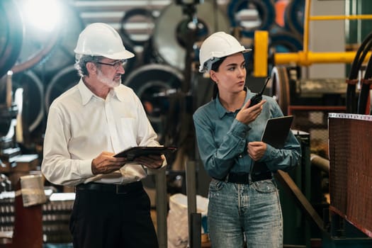 Factory engineer manager with assistant using laptop to conduct inspection of steel industrial machine, exemplifying leadership as machinery engineering inspection supervisor in metalwork manufacture.