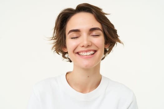 Close up portrait of brunette girl with short haircut, smiling and looking happy, posing over white background.