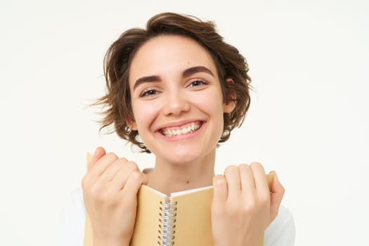 Portrait of happy, beautiful woman holding planner, making notes, doing her homework, standing over white background.