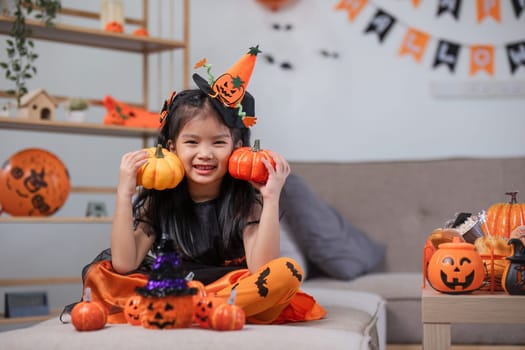 Cute little girl wearing a Halloween costume holding a pumpkin at home with happy eyes. looking at the camera..