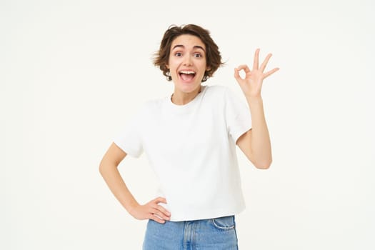 No problem. Portrait of young woman standing in confident pose, shows okay, ok, zero gesture, stands over white studio background.