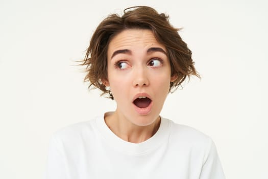 Close up shot of woman with shocked face, gasping and staring startled at camera, confused and surprised by something, standing over white background.