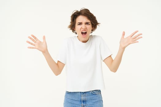 Portrait of disappointed, upset young woman shaking hands, shouting, complaining, shaking hands and looking frustrated, standing over white background.