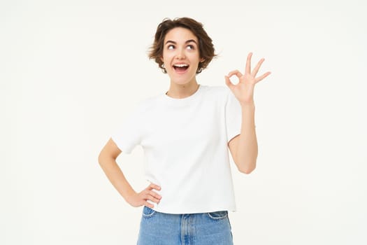 No problem, excellent. Young happy woman shows ok, okay gesture, nod in approval, recommending something good, standing over white background.