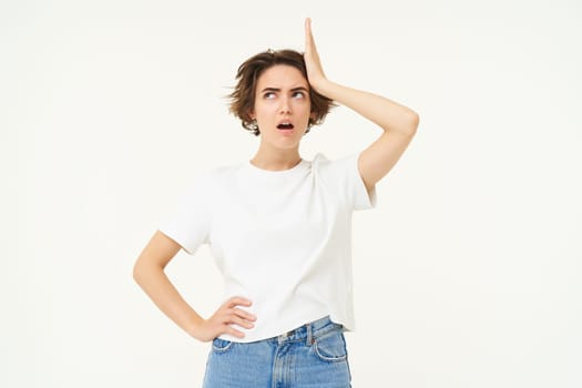 Portrait of forgetful woman, touches her head, remember something important, looks upset or shocked, stands over white background.