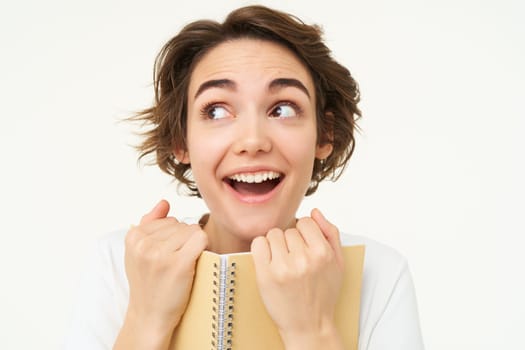 Portrait of happy woman with planner, holding notebook, reading notes and smiling, standing over white background.