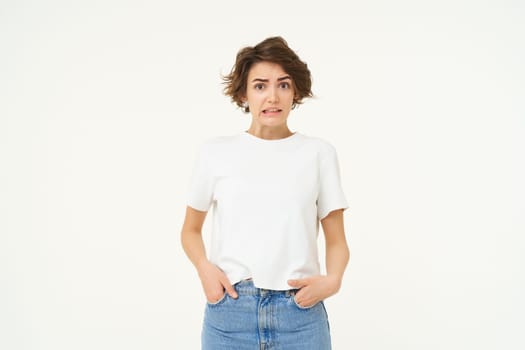 Portrait of girl with concerned face, looks unsure, grimacing, looking confused, standing over white background.