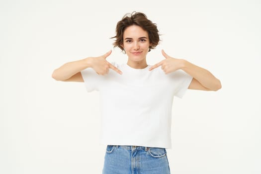 Image of confident, happy young woman, pointing at herself with smiling face, self-assured, standing over white background.