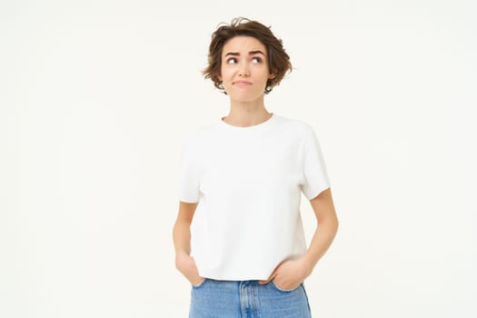 Portrait of confused brunette woman, looks up, thinking, looks unsure, standing in doubt against white background.