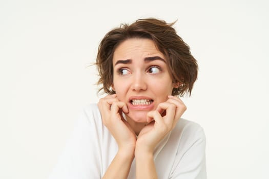 Close up of scared brunette woman, shaking from fear, looking concerned and frightened, standing over white studio background.