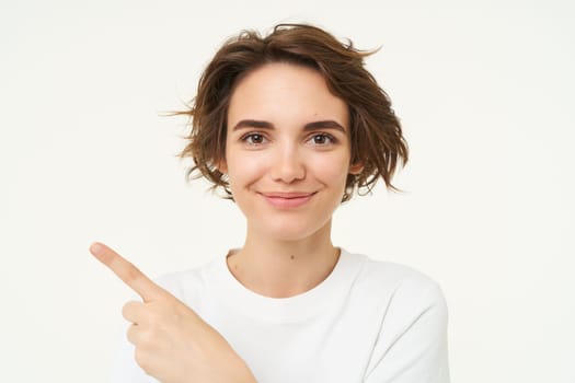 Close up shot of happy, candid woman, laughing and smiling, pointing finger left, showing advertisement, standing over white background.