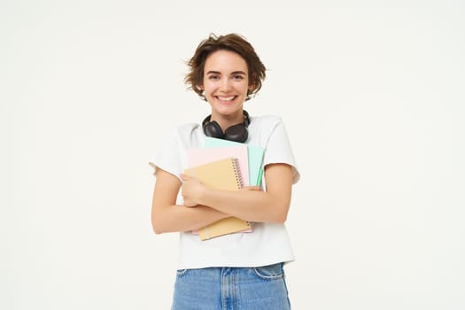 Portrait of candid young woman, student with notebooks, smiling and looking with confidence at camera, studying, standing over white background.