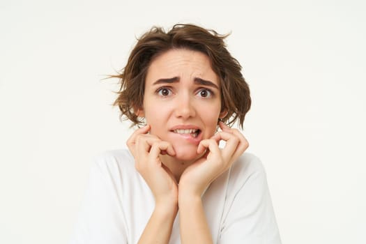 Close up of scared brunette woman, shaking from fear, looking concerned and frightened, standing over white studio background.