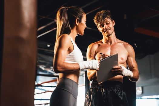 Asian female Muay Thai boxer and her personal boxing trainer discussing on her physical progress in the gym reflecting commitment to her body muscle growth and boxing performance. Impetus