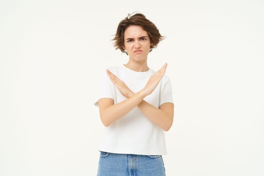 Portrait of woman with serious face, shows cross, stop gesture, prohibit something bad, standing over white background. copy space