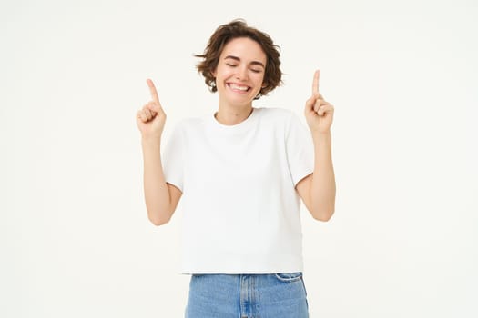 Image of happy, beautiful modern woman, pointing fingers up, showing advertisement on top, smiling, standing over white background.