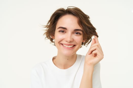 Close up portrait of brunette woman smiling, playing with hair strand, showing new haircut, posing over white studio background. Copy space
