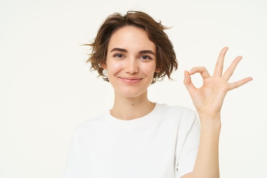 Close up of smiling, happy young woman shows zero, okay ok gesture, approve something good, standing over white background.