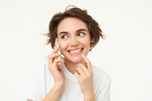 Image of smiling, brunette woman calling someone, talking on mobile phone, answer telephone call, standing over white background.