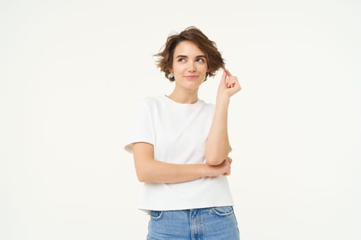 Portrait of thoughtful brunette girl, playing with her curl and thinking with smiling face, standing over white background.