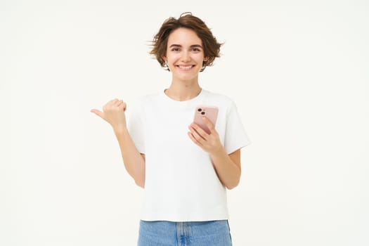 Portrait of woman with smartphone, using mobile phone and pointing at banner, showing text advertisement, standing isolated against white background.