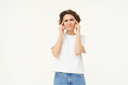 Image of distressed, upset young woman touches her head, has headache, suffers from migraine, stands over white background. Copy space