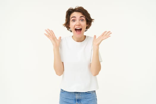 Portrait of surprised brunette woman looks surprised, gasping amazed, reacts to amazing big news, stands over white background.