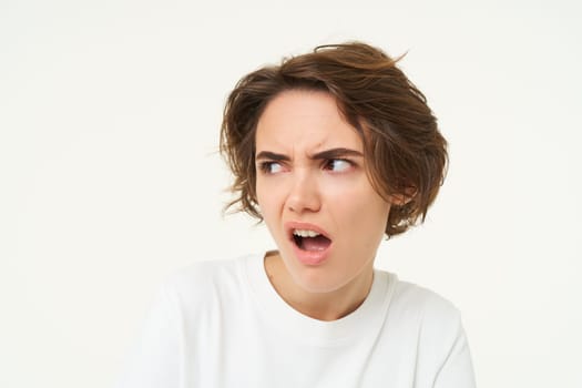 Portrait of offended woman, frowning and looking with dismay aside, complaining at someone, looks frustrated, stands over white background.