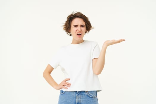 Portrait of woman complaining, raising hand up with frustration, looking angry, standing over white background. Copy space