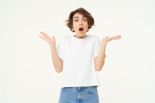 Surprised people. Young woman gasps, shrugs shoulders and looks impressed, amazed by something, isolated against white background.