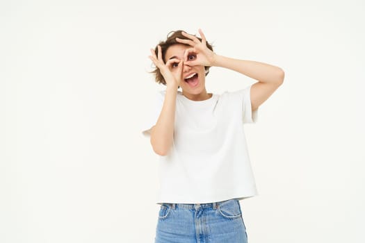Portrait of happy woman making fun hand glasses over eyes and laughing, isolated over white background.