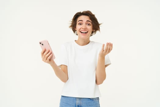 Technology and people. Happy brunette woman with mobile phone, smiling and laughing, standing over white background. Copy space