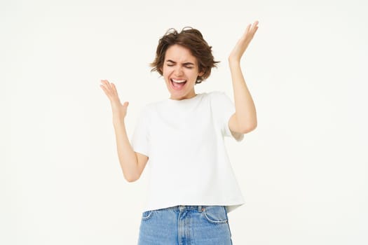 Portrait of woman celebrating, winning prize, triumphing, standing over white studio background.