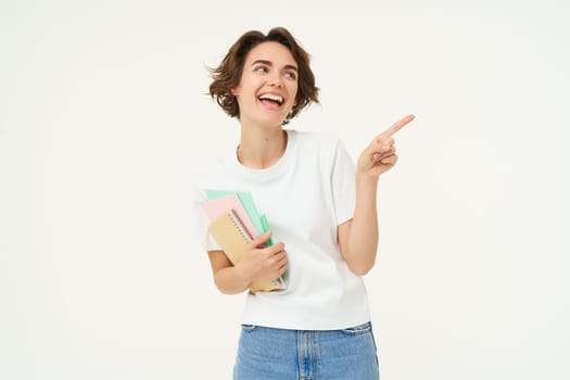 Portrait of woman laughing, pointing at upper right corner, showing promo banner, holding papers, documents and workbooks, white background.
