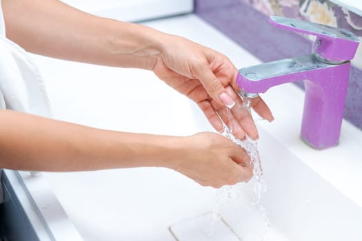 woman washes her hands under running water from a tap in the bathroom, concept of hygiene and protection from bacteria