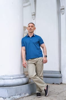 a man in casual clothes stands near the columns of a white building