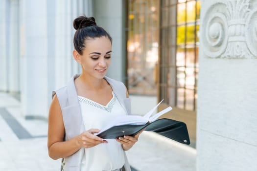 Beautiful woman smiling happy standing at city. Notepad in hand standing on street, in stylish clothes