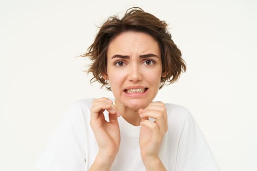 Close up portrait of woman cringing, looking disgusted, jumps from fear and looks afraid, stands over white background. Copy space