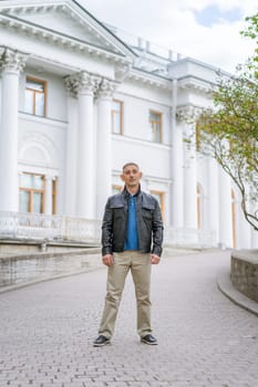 a man in casual clothes stands near a beautiful white building