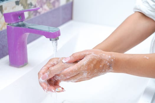 woman washes her hands under running water from a tap in the bathroom, concept of hygiene and protection from bacteria